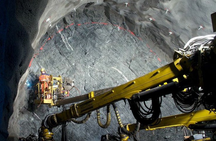 A worker beside drilling equipment in an underground industrial environment